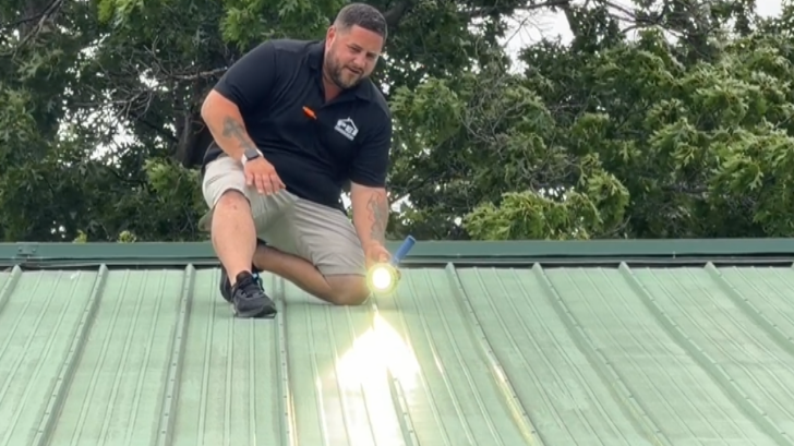 PEI salesmen Jason Lundeen on green metal roof inspecting for storm damage