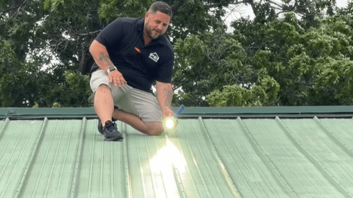 Minnesota General Contractor Sales Representative Jason Lundeen shining flashlight down a metal roof inspecting for hail damage